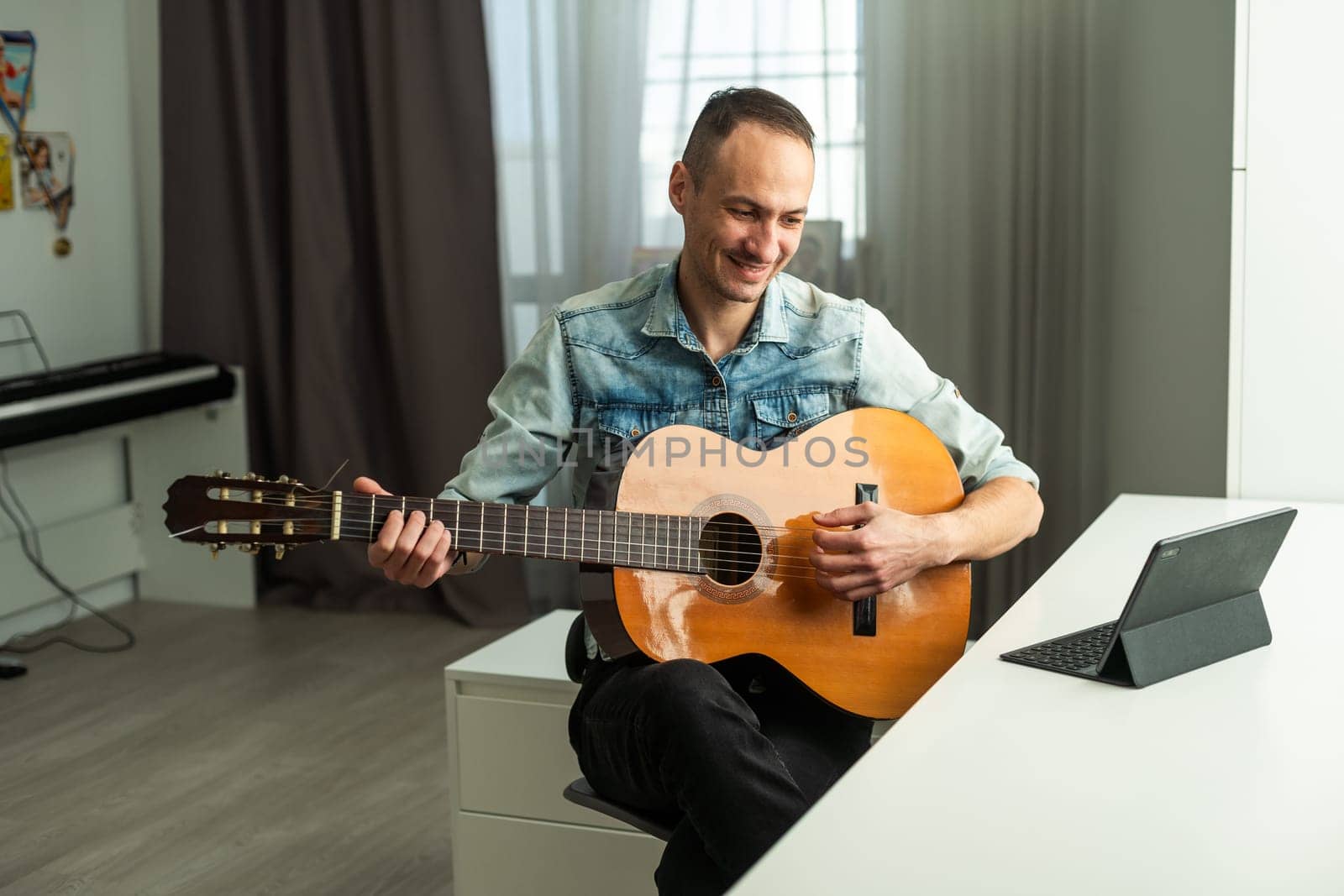 Portrait of man taking online guitar lesson looking at laptop screen. Retired male learning to play guitar watching webinar on computer at home. High quality photo