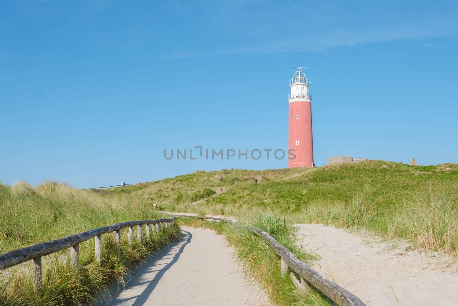 A winding path through the sandy dunes leads to a picturesque lighthouse standing tall against the horizon in Texel, Netherlands.
