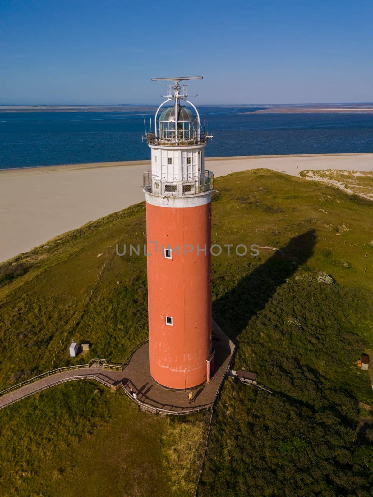 An aerial perspective capturing a lone lighthouse standing tall on the sandy shore of Texel, Netherlands, guiding ships safely through the night.