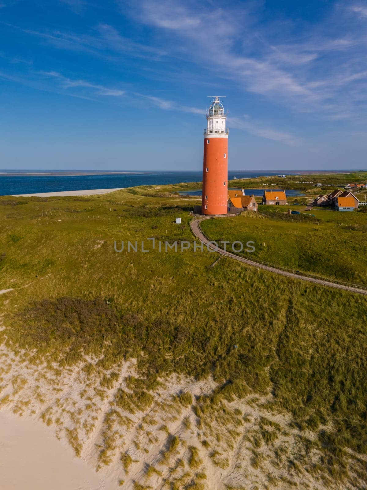 A stunning aerial view of a lighthouse standing tall on a sandy beach, shining a light to guide ships safely to shore.