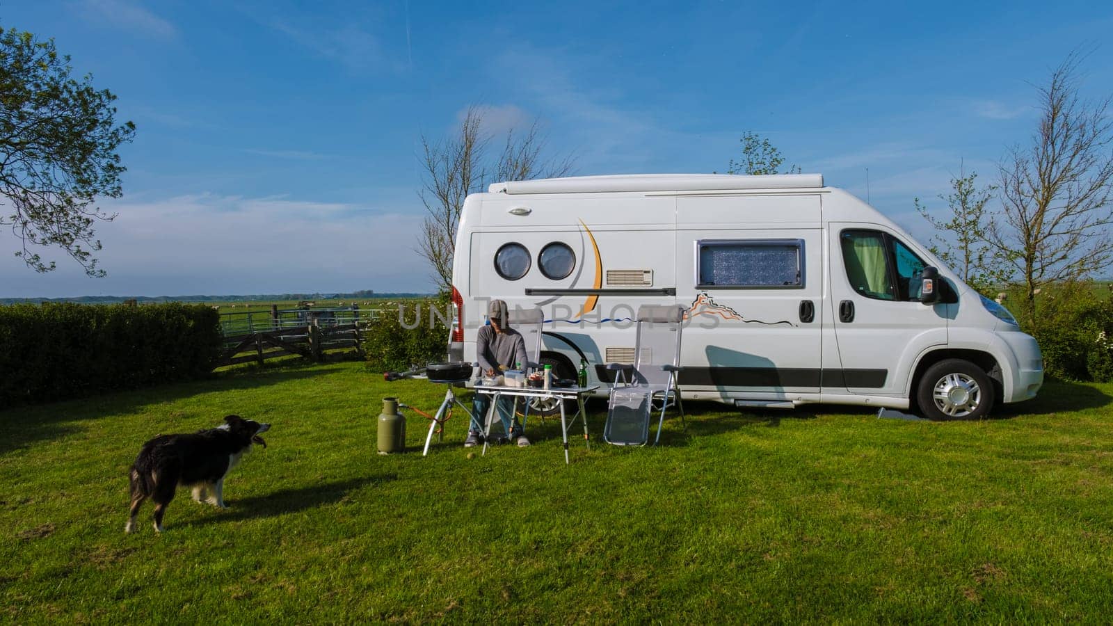 A brown dog sits contentedly on the grass beside a vibrant RV against a backdrop of Texel, Netherlands. camping at a farm in Texel Netherlands