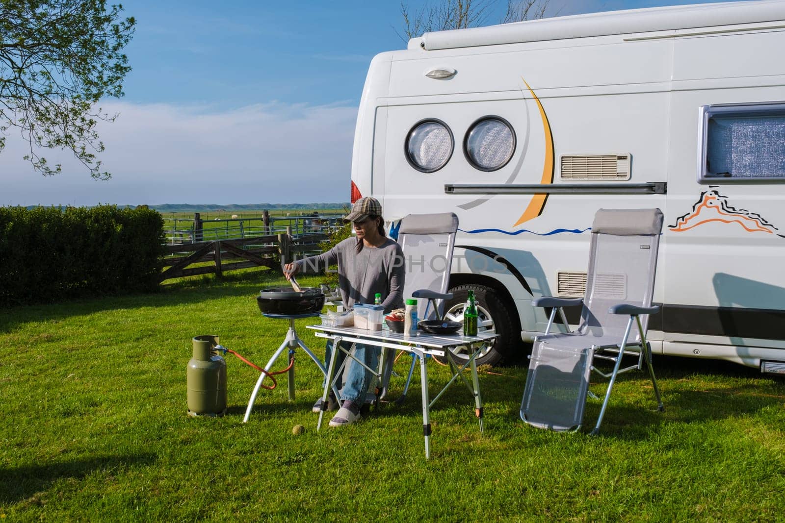 A woman sits at a table next to an RV in Texel, Netherlands, enjoying the peace and quiet of the countryside.