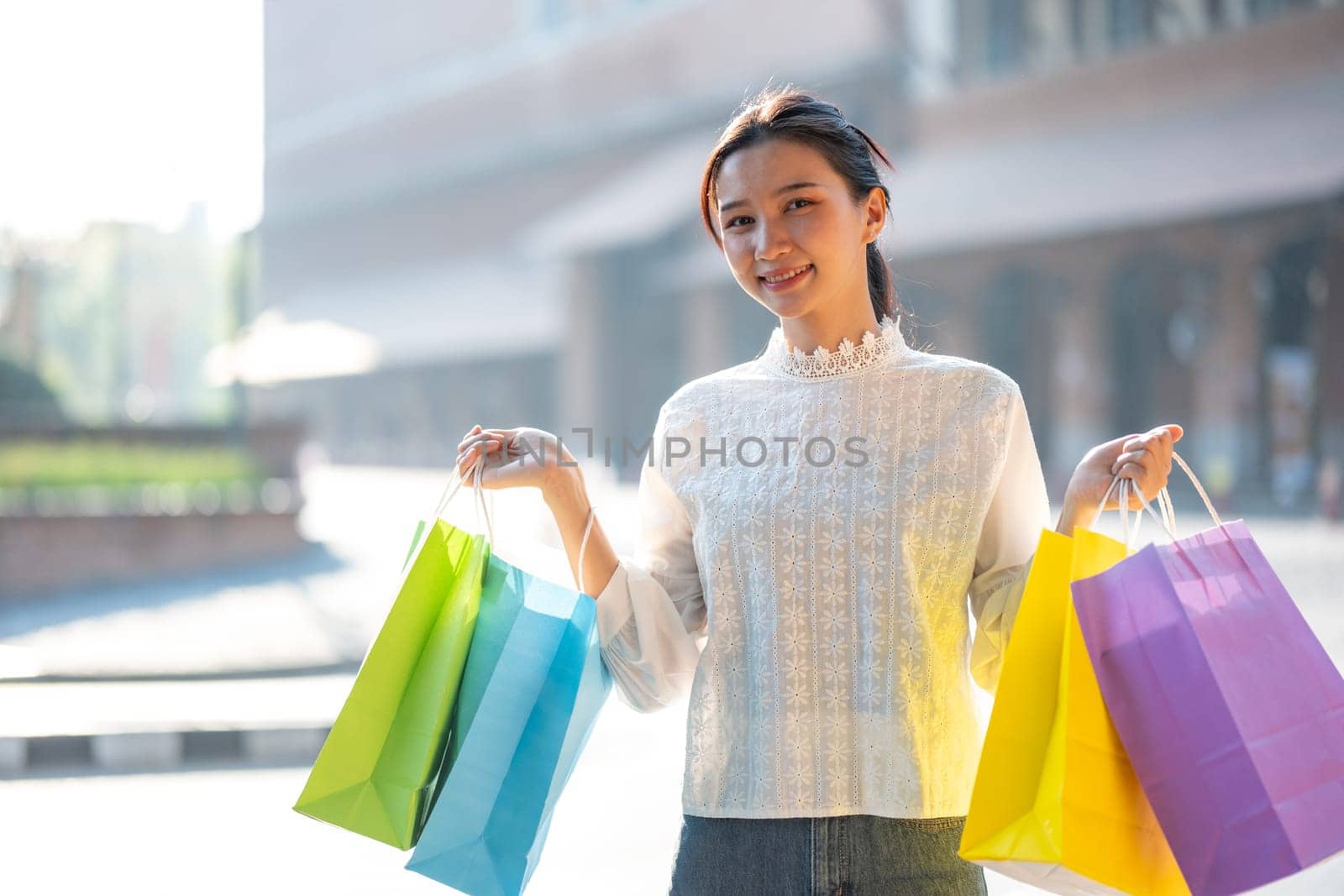 Cheerful young woman enjoying a shopping spree, holding colorful shopping bags in a sunny outdoor setting.