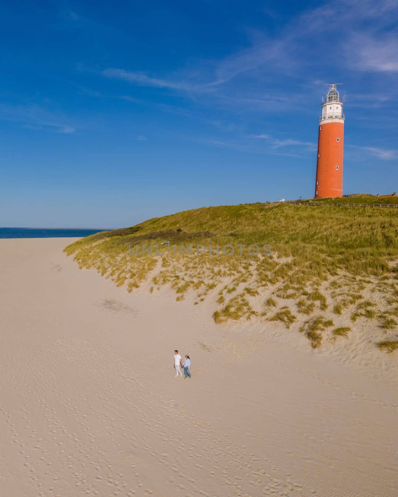 An aerial view of a majestic lighthouse standing tall on the Texel, Netherlands beach, surrounded by golden sand and the soothing waves of the sea.