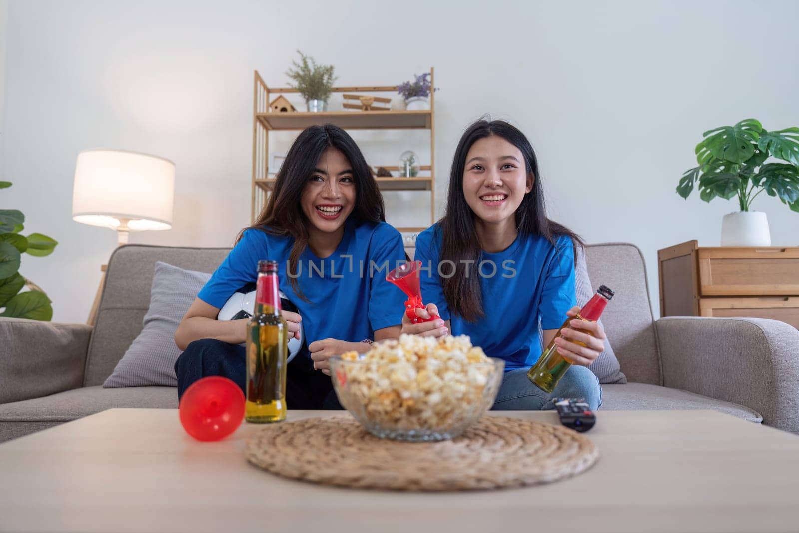 Lesbian couple cheering for Euro football with drinks and popcorn at home. Concept of sports enthusiasm and LGBTQ pride.