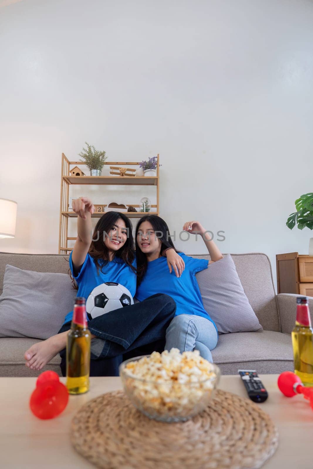 Lesbian couple cheering for Euro football at home with popcorn and drinks. Concept of sports enthusiasm and LGBTQ pride.