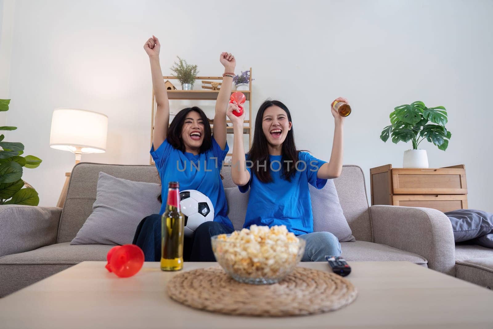 Lesbian couple cheering for Euro football with drinks and popcorn at home. Concept of sports enthusiasm and LGBTQ pride.