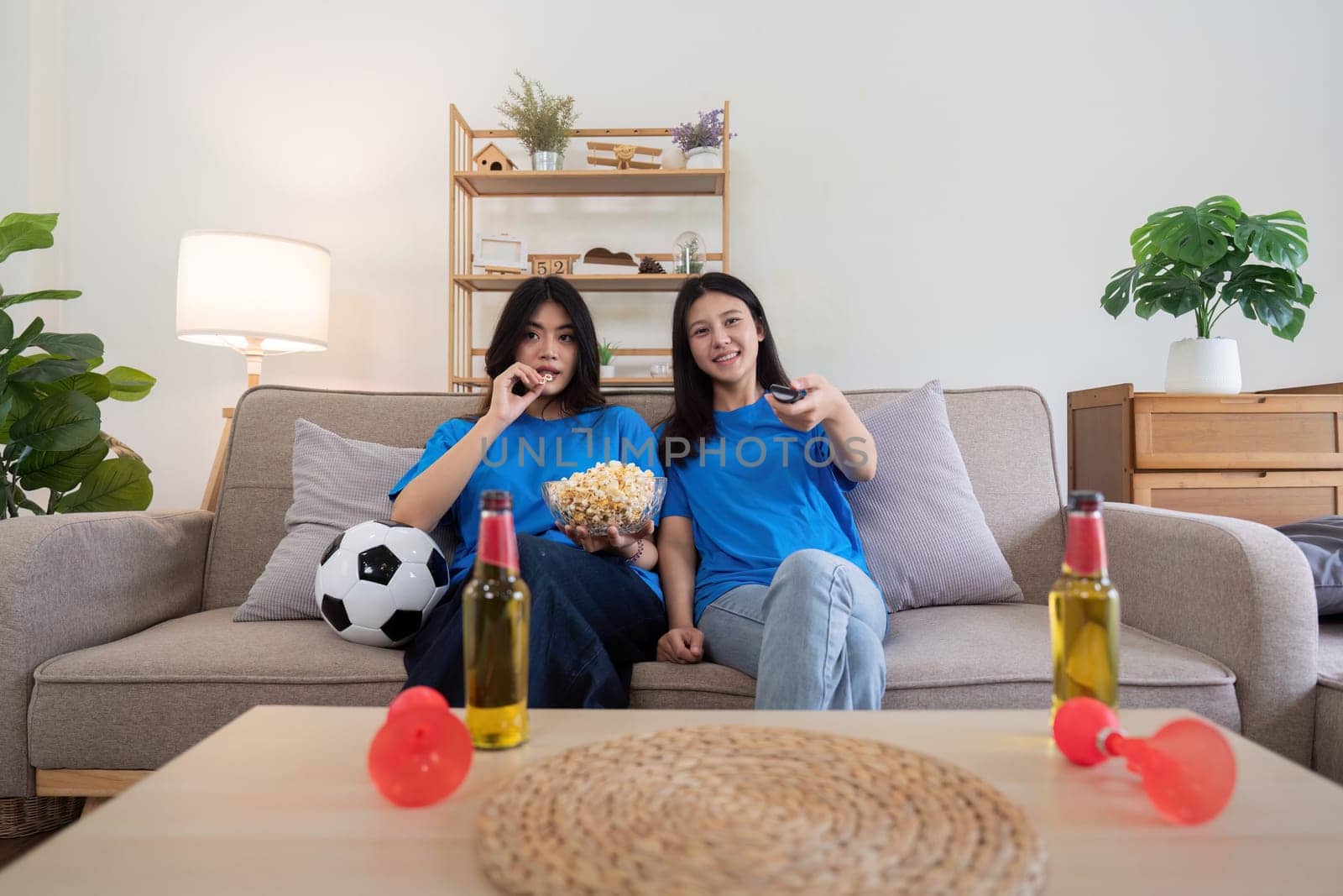 Lesbian couple cheering for Euro football at home with popcorn and drinks. Concept of sports enthusiasm and LGBTQ pride by nateemee