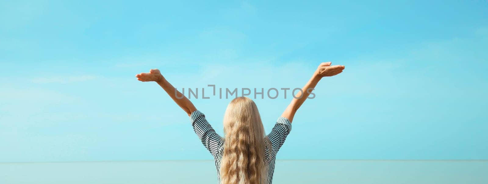 Summer vacation, happy young woman raising her hands up on the beach on sea coast and blue sky background