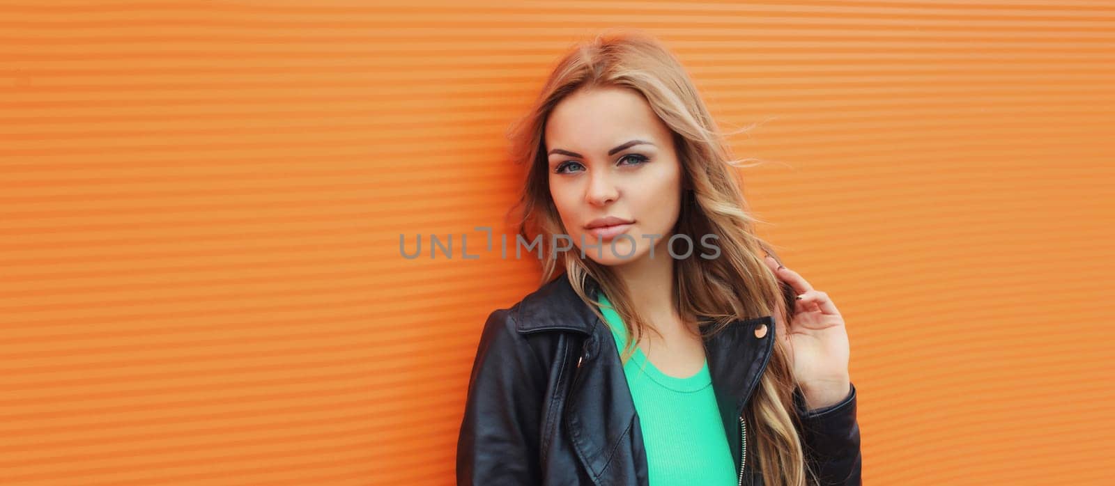 Portrait beautiful young blonde woman posing in black leather jacket on colorful orange background by Rohappy
