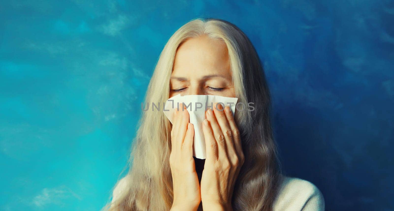 Sick exhausted middle aged woman sneezing blow nose using tissue at home