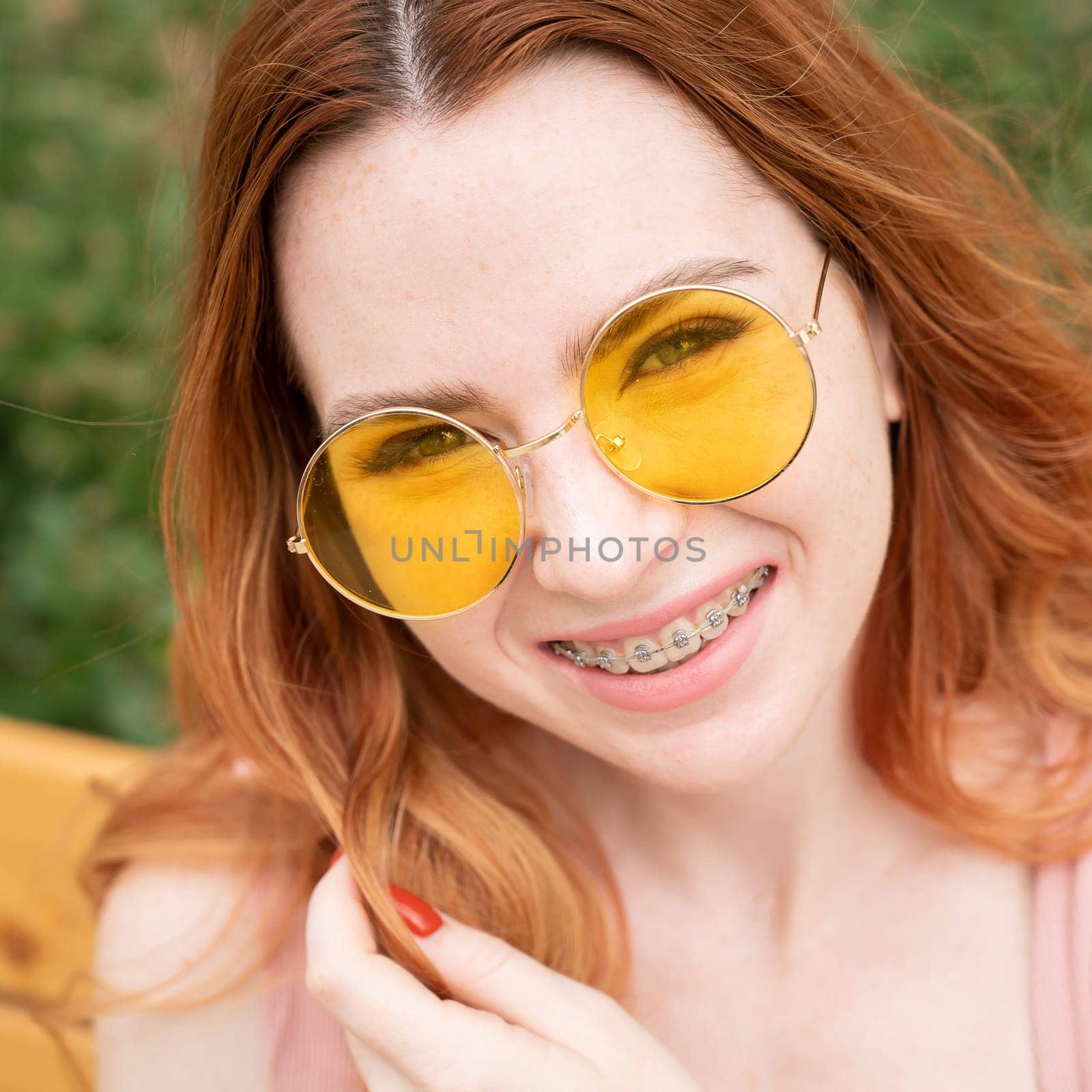Beautiful young woman in yellow sunglasses smiling showing off braces on her teeth