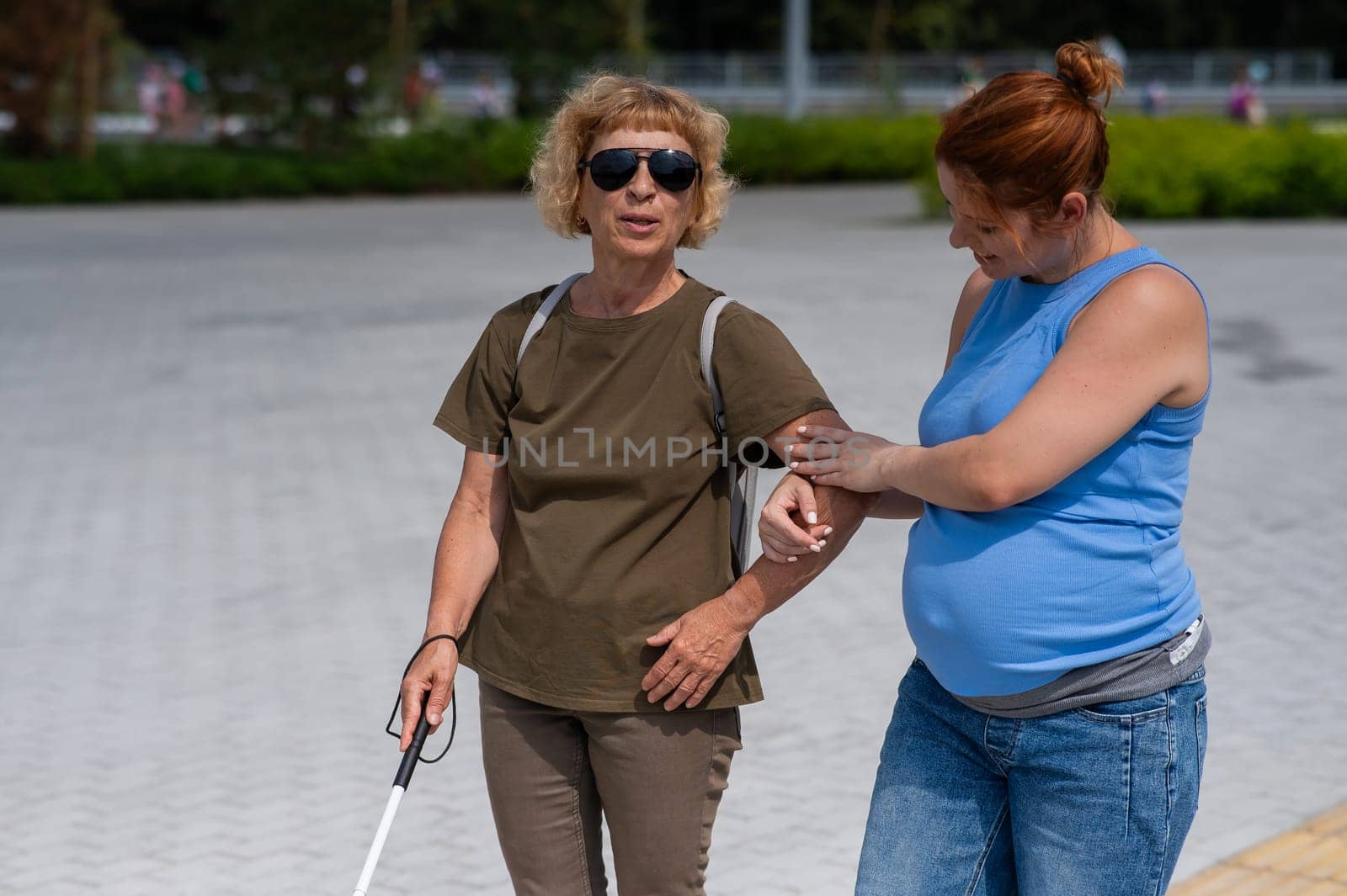 Caucasian pregnant woman leading blind elderly lady outdoors. by mrwed54