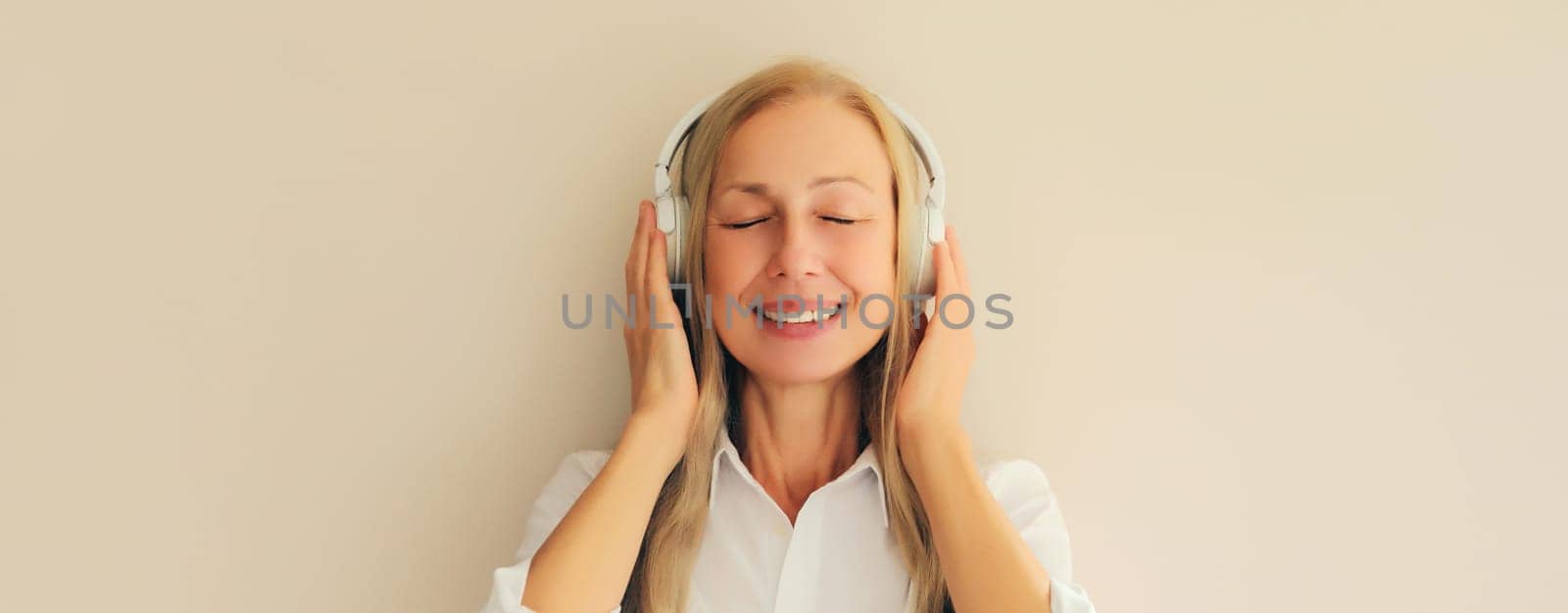 Portrait of happy relaxed middle aged woman listening to music in wireless headphones on white background