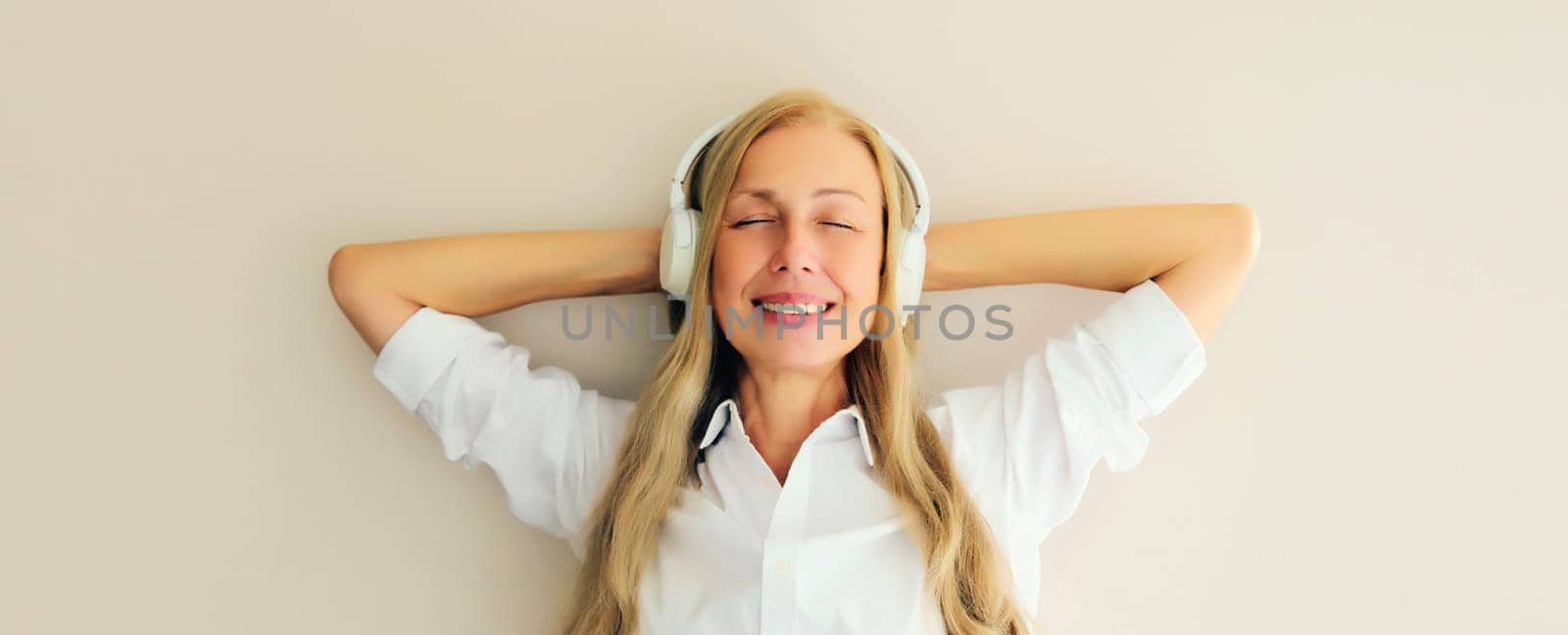 Portrait of happy relaxed middle aged woman listening to music in wireless headphones on white background