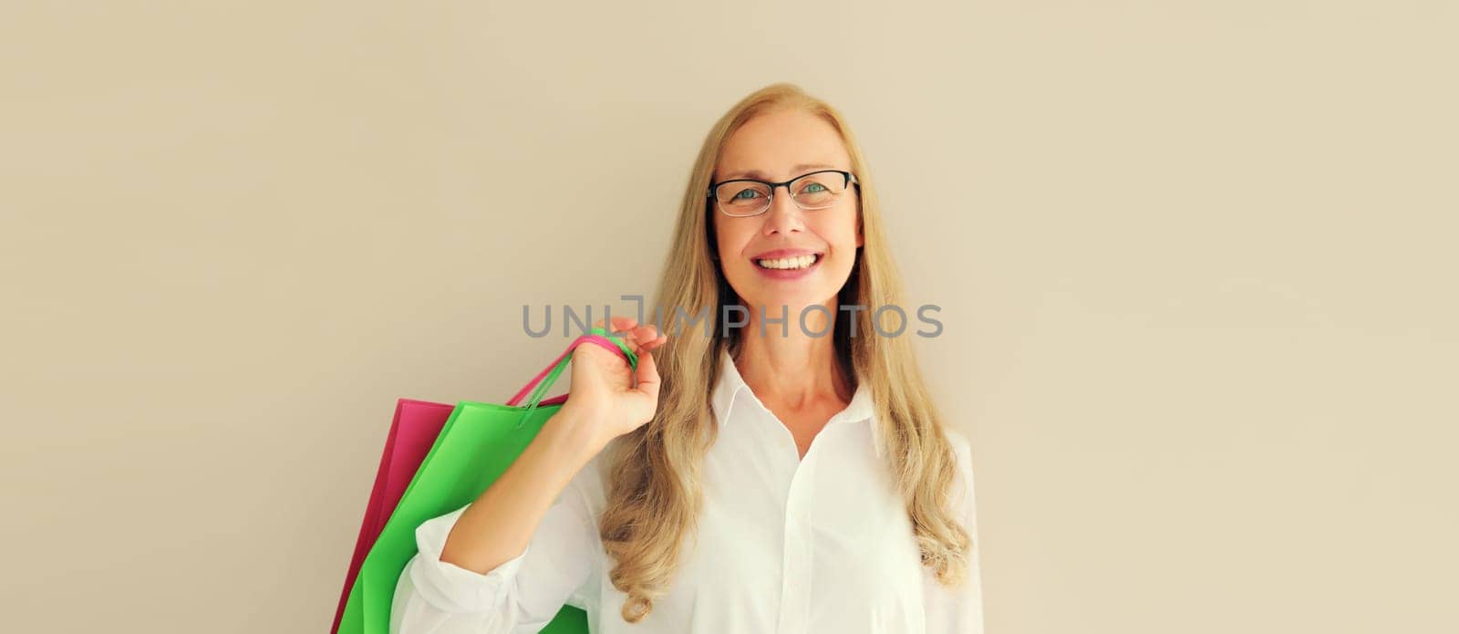 Portrait of beautiful happy smiling middle aged woman posing with colorful shopping bags in eyeglasses on studio background