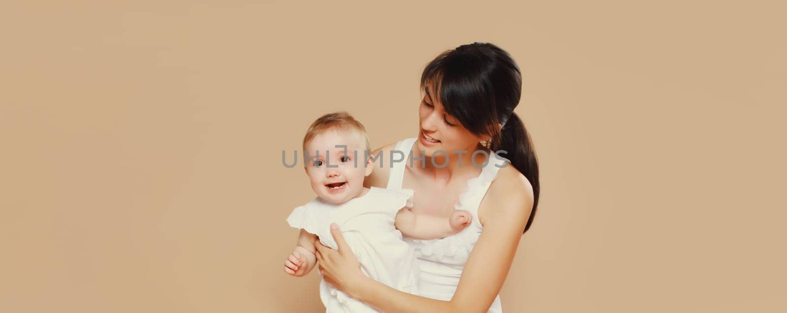 Happy cheerful smiling young mother playing with cute baby on brown studio background