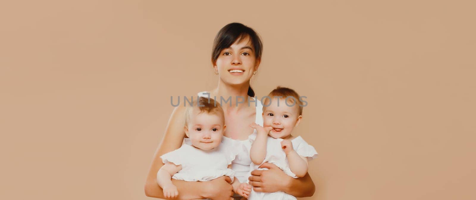 Happy cheerful smiling young mother holding baby on brown studio background