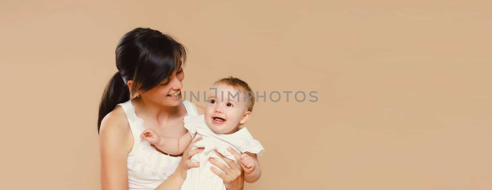 Happy cheerful young mother playing with cute baby on brown studio background by Rohappy