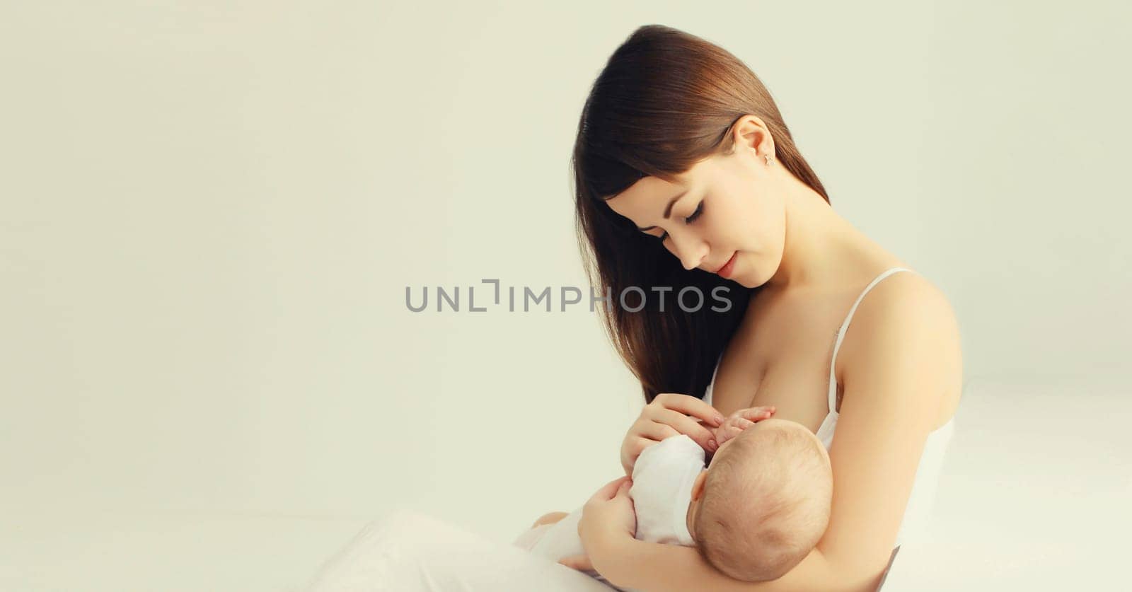 Portrait of happy young mother breastfeeding her baby at home on white background