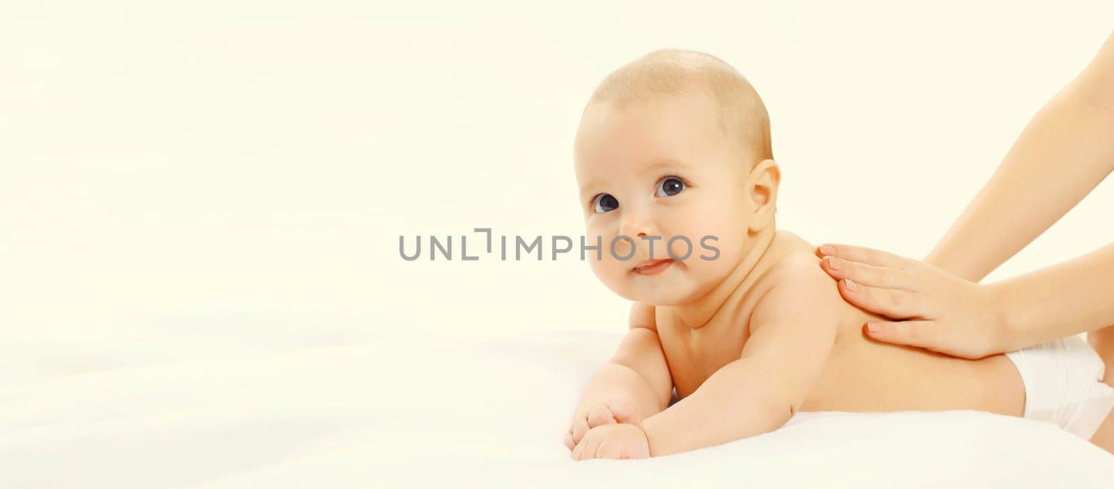 Close up mother gives massage to baby lying on the bed on white background, child and health concept