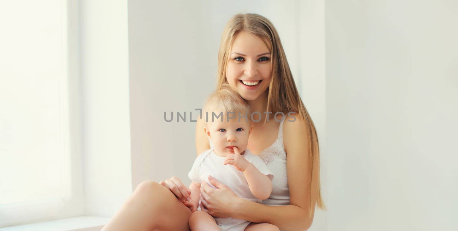 Happy smiling young mother playing with baby in white room at home by Rohappy