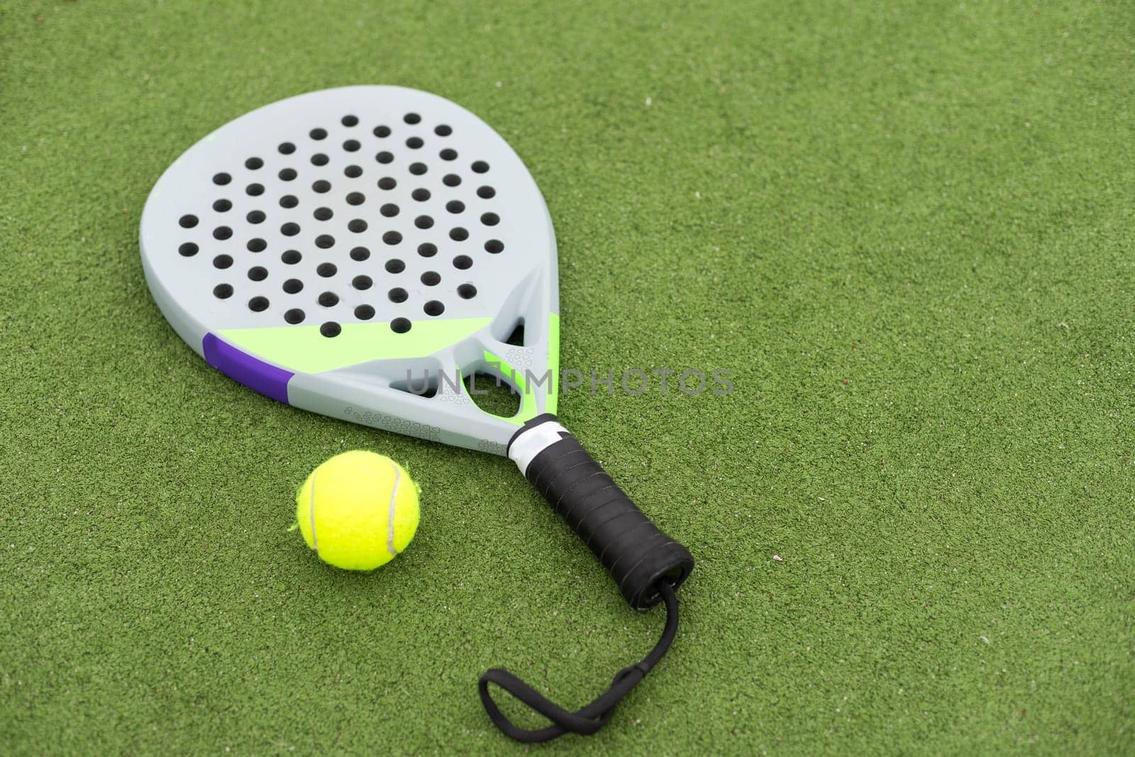 Padel racket and padel ball on a green court in the sunset. High quality photo