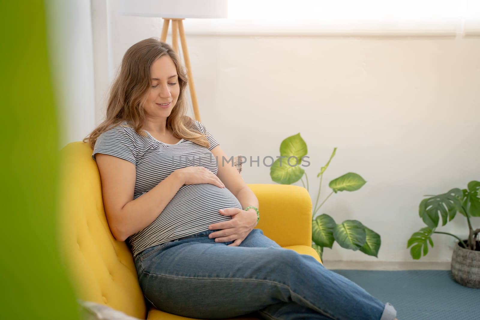 Pregnant woman embracing belly in living room. High quality photo