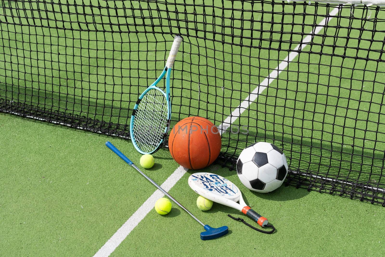 A variety of sports equipment including an american football, a soccer ball, a tennis racket, a tennis ball, and a basketball. High quality photo