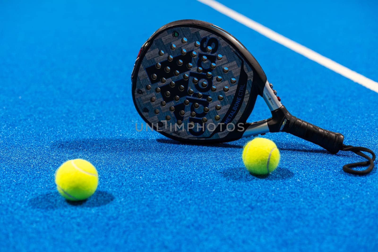 Kyiv, Ukraine, April 18, 2024. Black professional paddle tennis racket and ball with natural lighting on blue background. Horizontal sport theme poster, greeting cards, headers, website and app. High quality photo