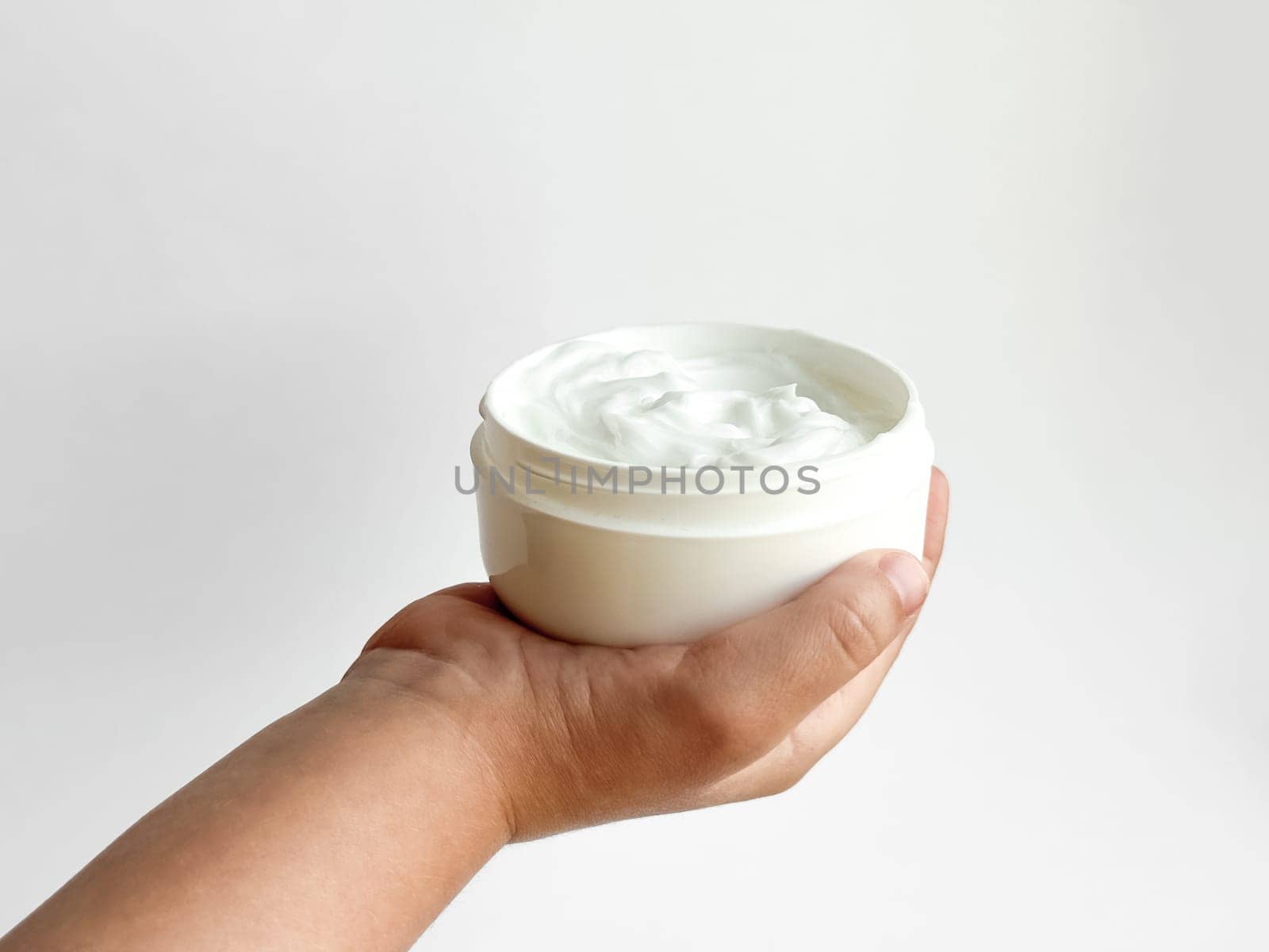 Close up of childs hand holding container of cream on white background with copy space. Skincare and moisturizing concept. Design for healthcare, wellness, and child care poster. High quality photo