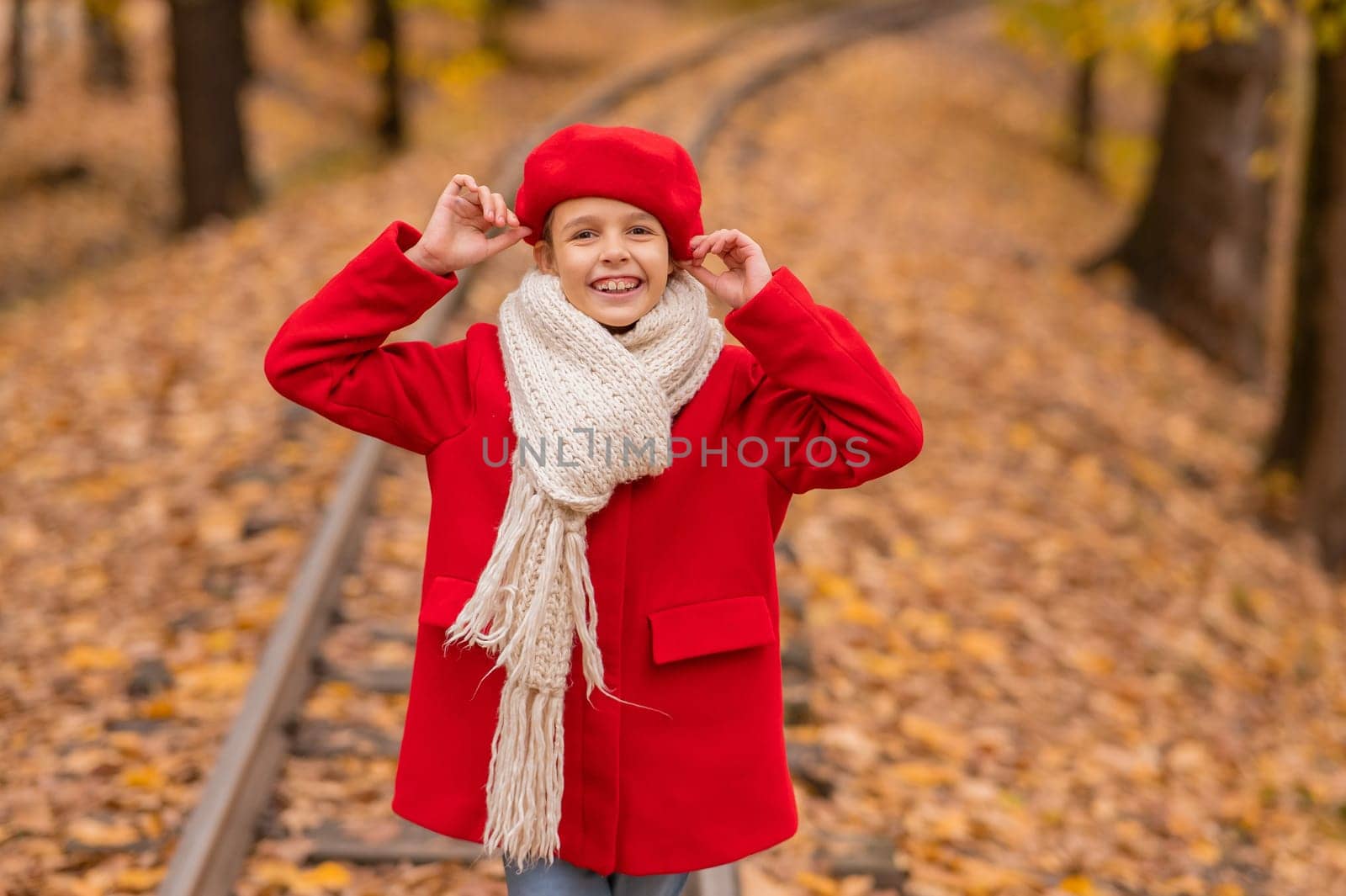 Caucasian girl in a red coat and beret walks along the railway tracks in the park in autumn