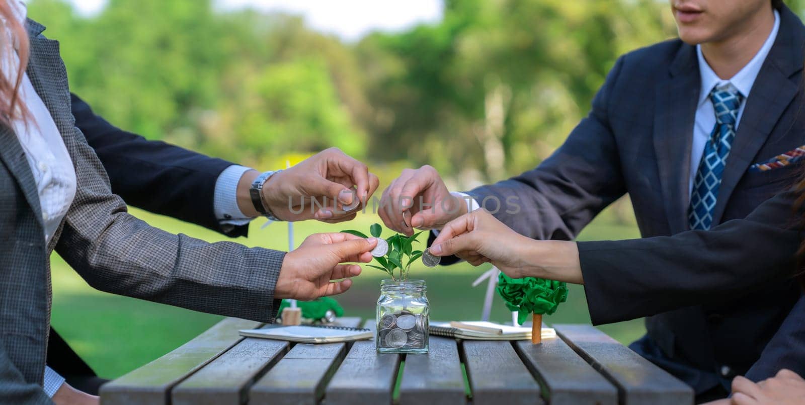 Business people put coin to money saving glass jar on outdoor table as sustainable money growth investment or eco-subsidize. Green corporate promot and invest in environmental awareness. Gyre