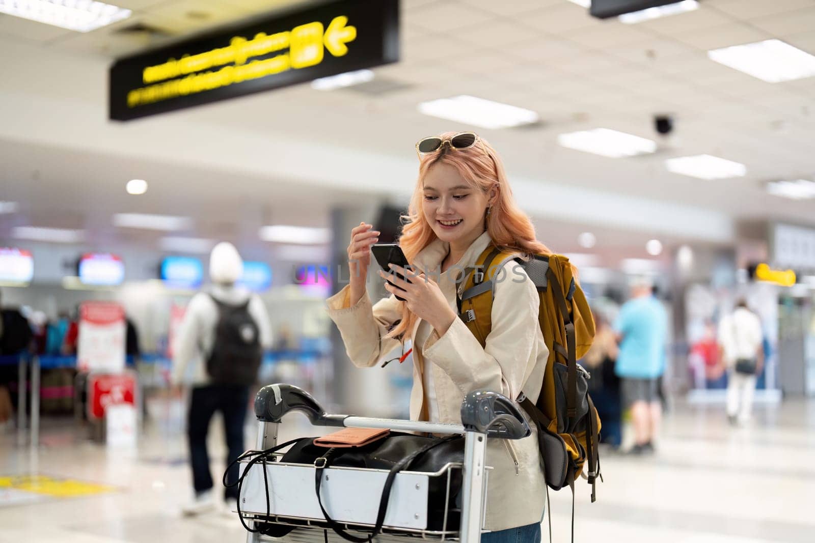 Young woman using smartphone at airport arrivals. Casual travel, checking messages, waiting for journey by nateemee