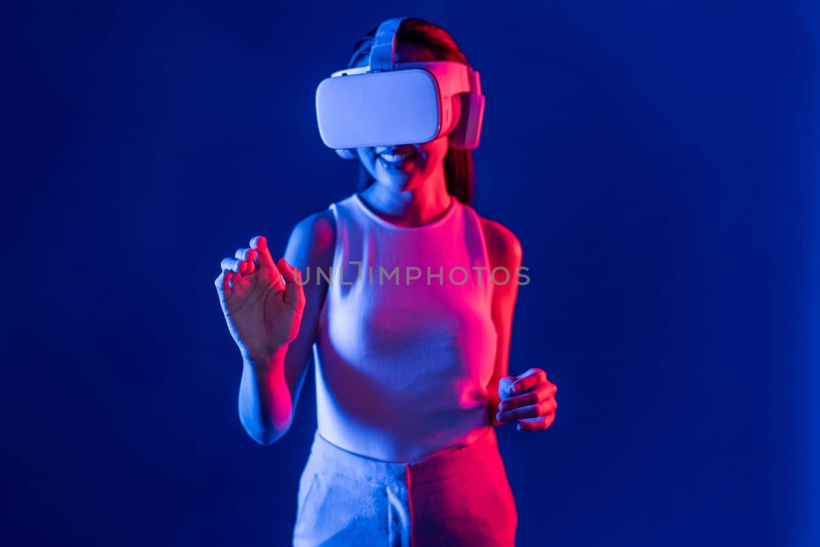 Smart female standing with surrounded by cyberpunk neon light wear VR headset connecting metaverse, futuristic cyberspace community technology. Woman using hand touching virtual object. Hallucination.