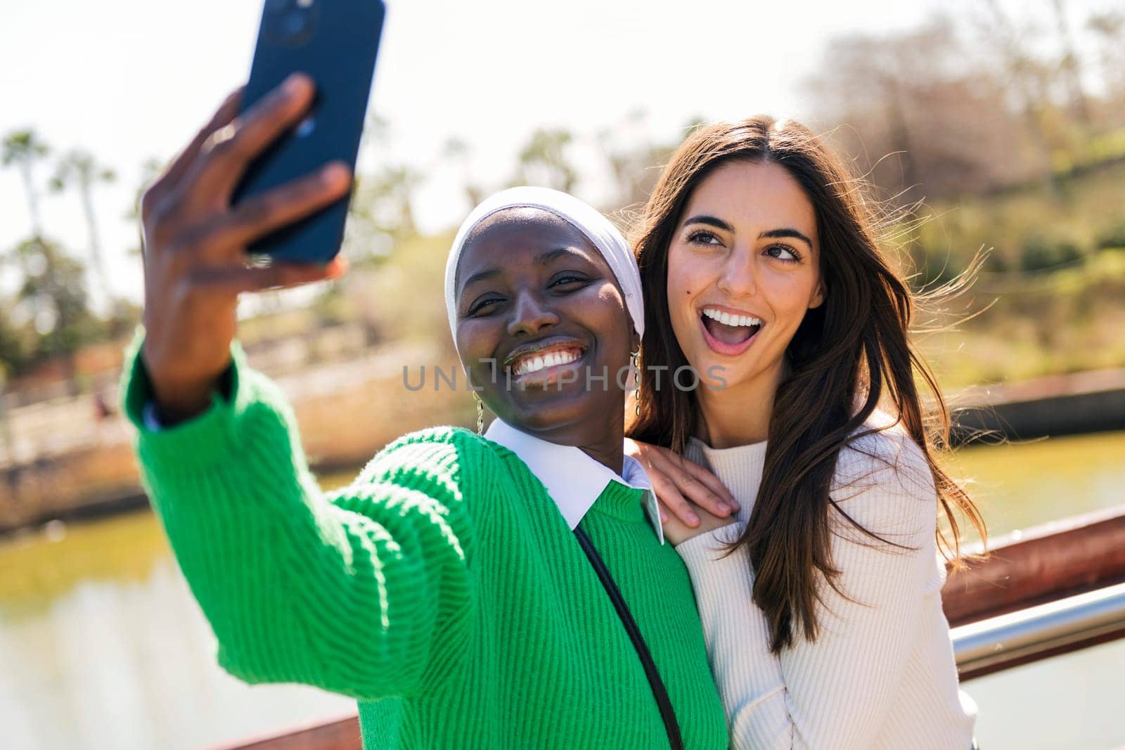 two young female friends smiling happy while having fun taking selfie photo with mobile phone in a city park, concept of friendship and modern lifestyle