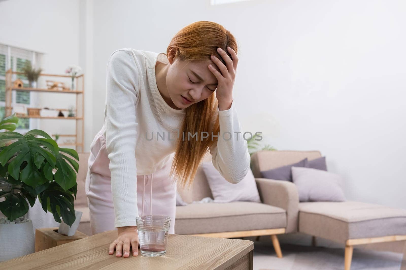 A young Asian woman in the living room was suffering from a headache due to accumulated stress due to health problems and lifestyle problems causing stress disorder. by wichayada