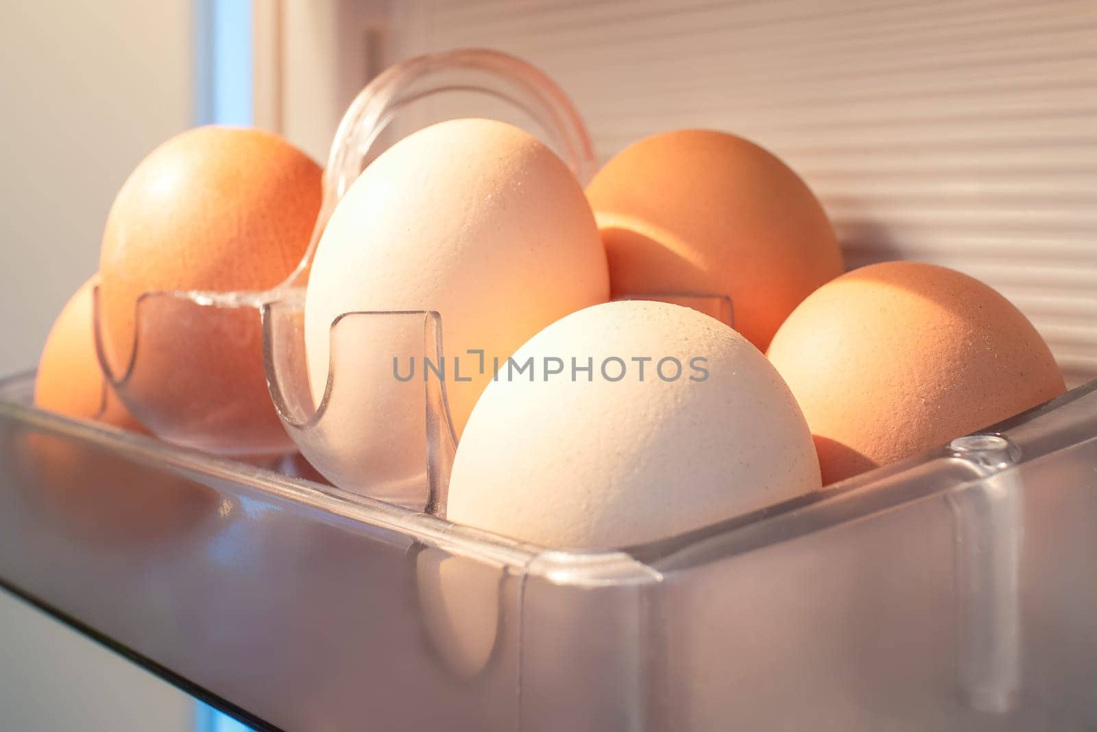 Organic eggs are stored in a transparent container inside a fridge, used as a key ingredient in various dishes, an oval staple food in different cuisines