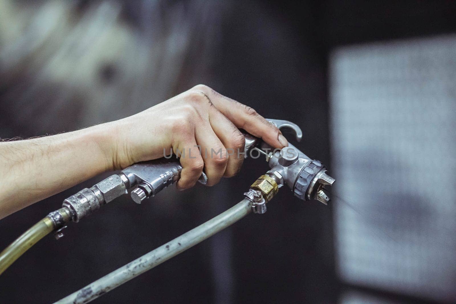 A worker paints with a spray gun at a factory. Close-up.