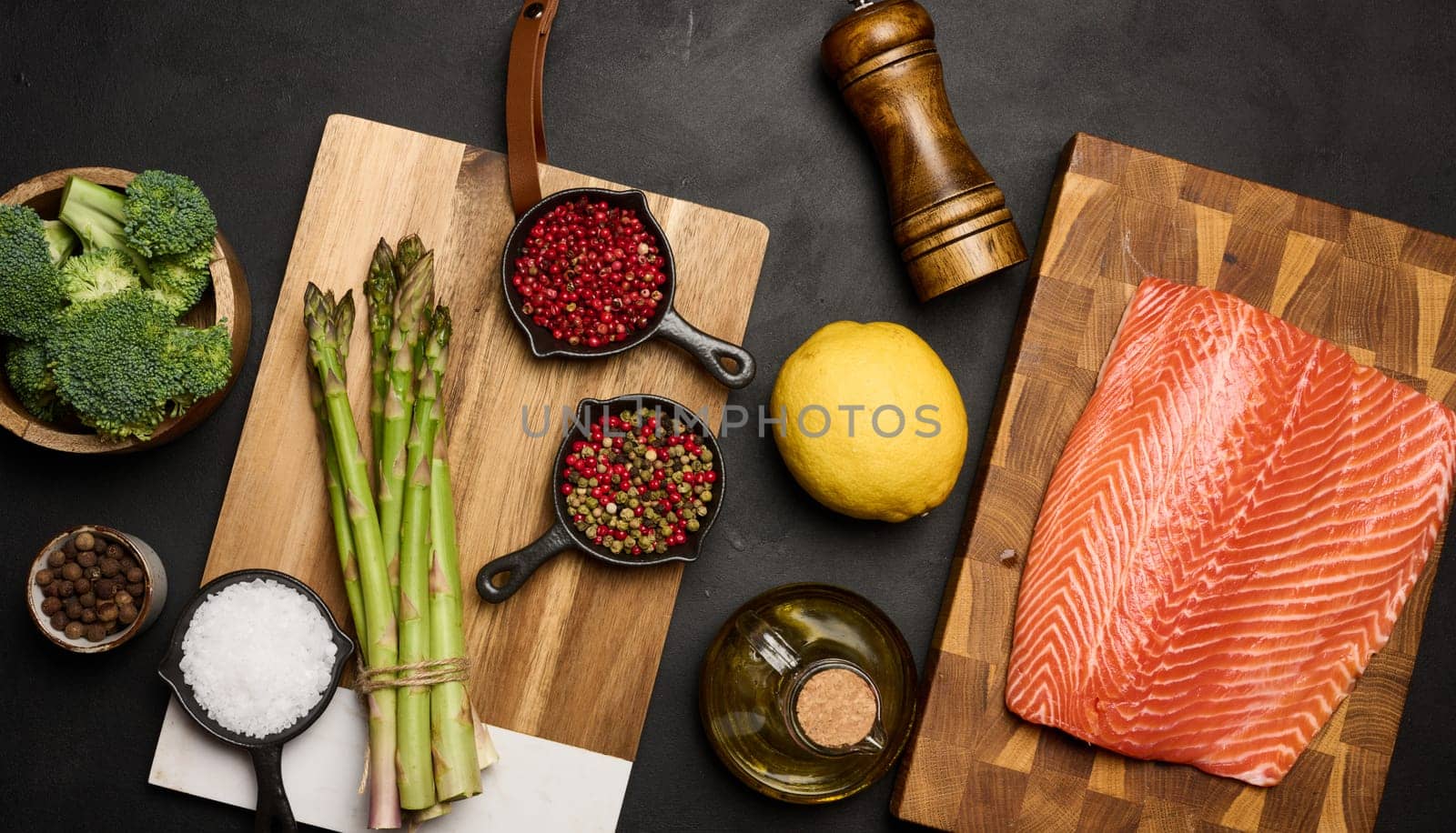 A piece of raw trout fillet on a wooden board, next to asparagus and broccoli. View from above