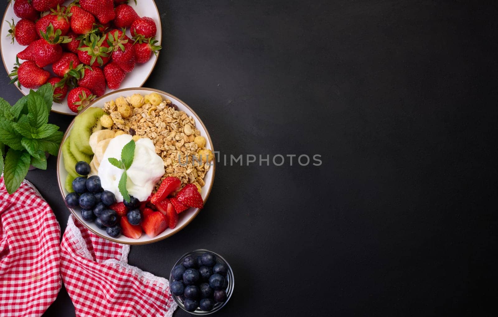 Healthy breakfast. Granola with strawberries, kiwi, banana and blueberries in a round plate on a black table. Healthy and tasty food, copy space