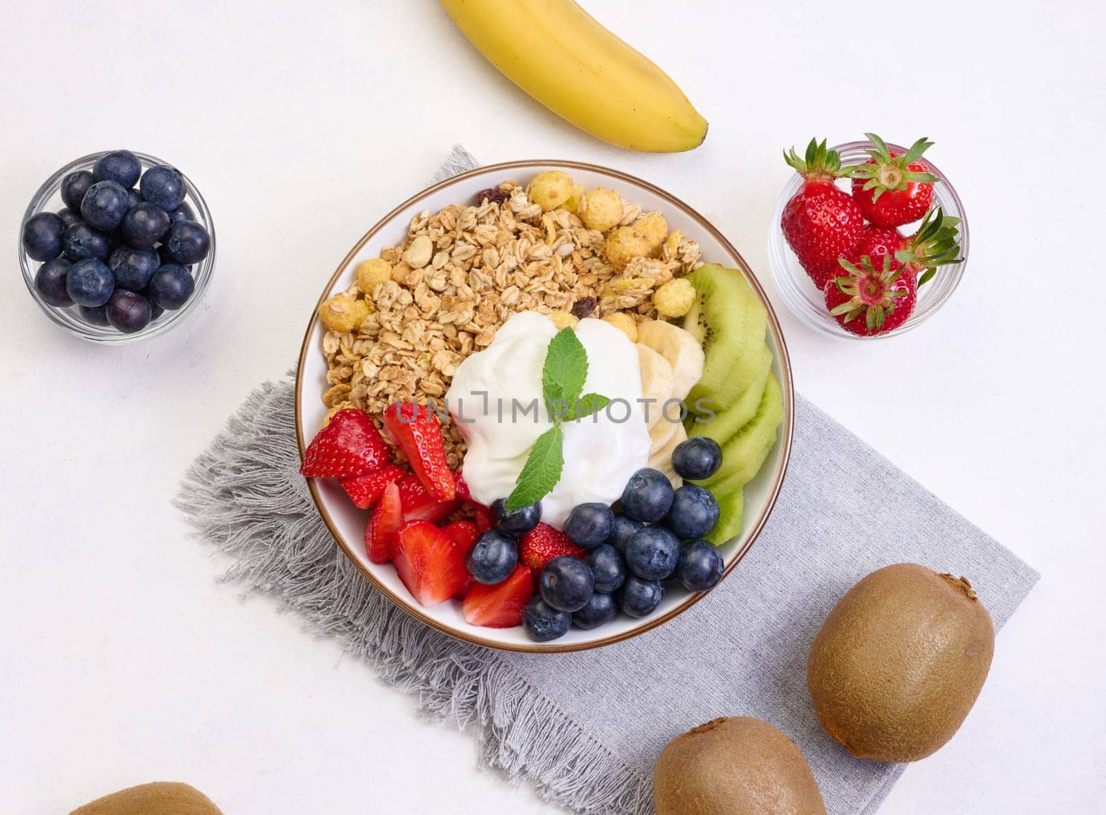 Granola with strawberries, kiwi, banana and blueberries in a round plate on a white table.  by ndanko