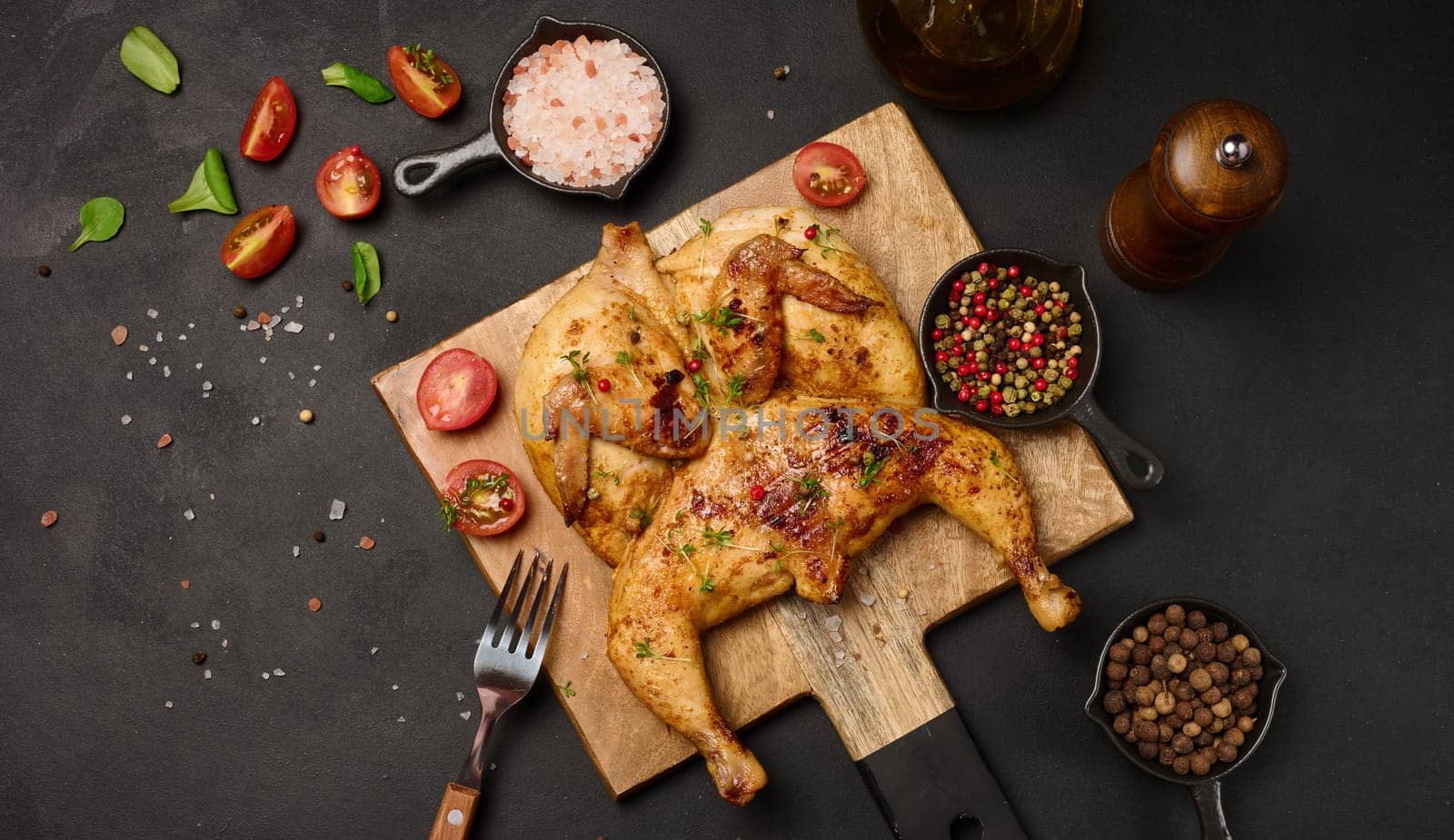 Whole fried chicken with spices on a wooden board on a black table by ndanko