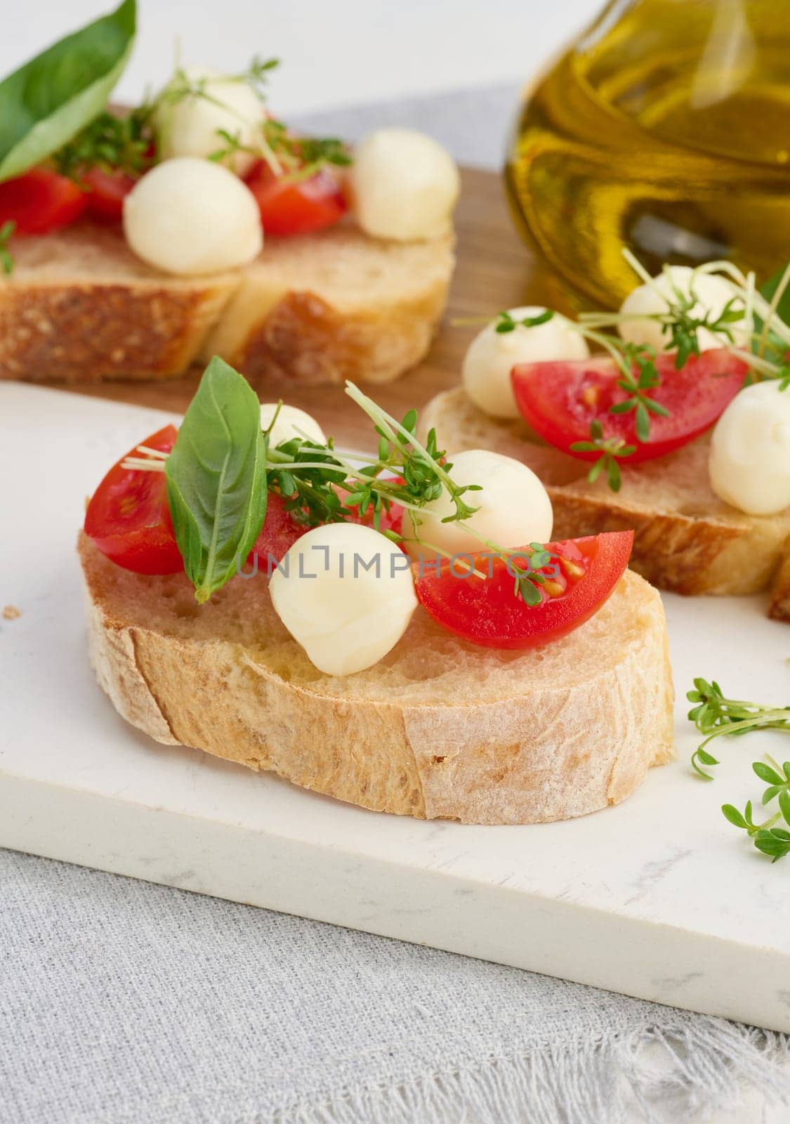 Round mozzarella, cherry tomatoes and microgreens on a piece of white bread, close up