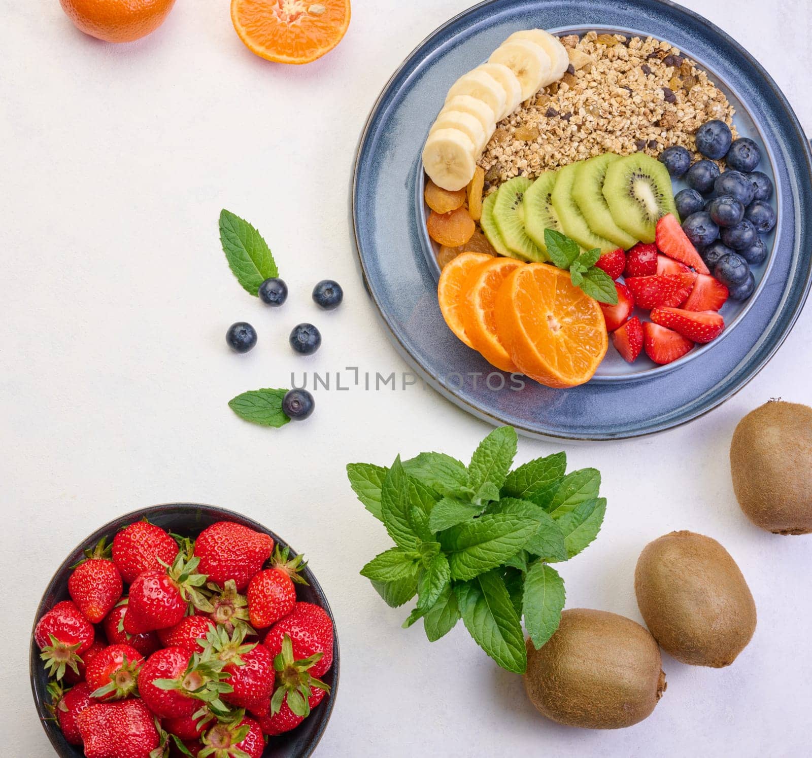 Granola with strawberries, kiwi, banana and blueberries in a round plate on a white table. Healthy and tasty food, top view