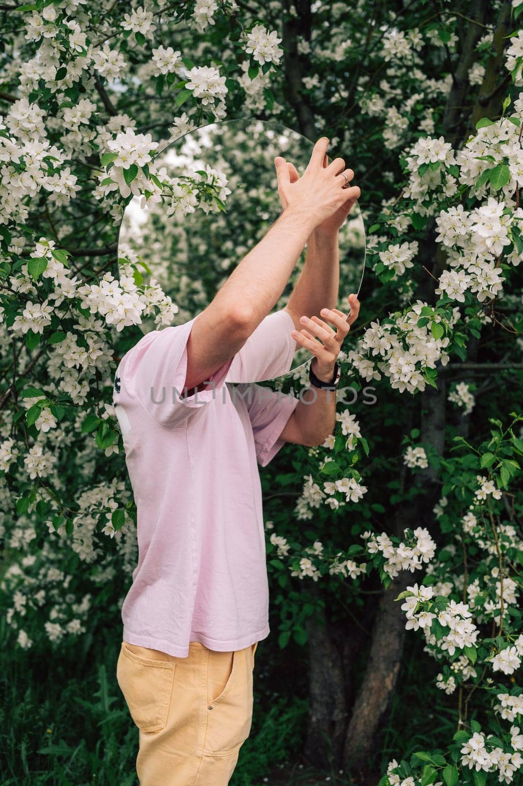 Creative male portrait with mirror in a blooming apples spring garden