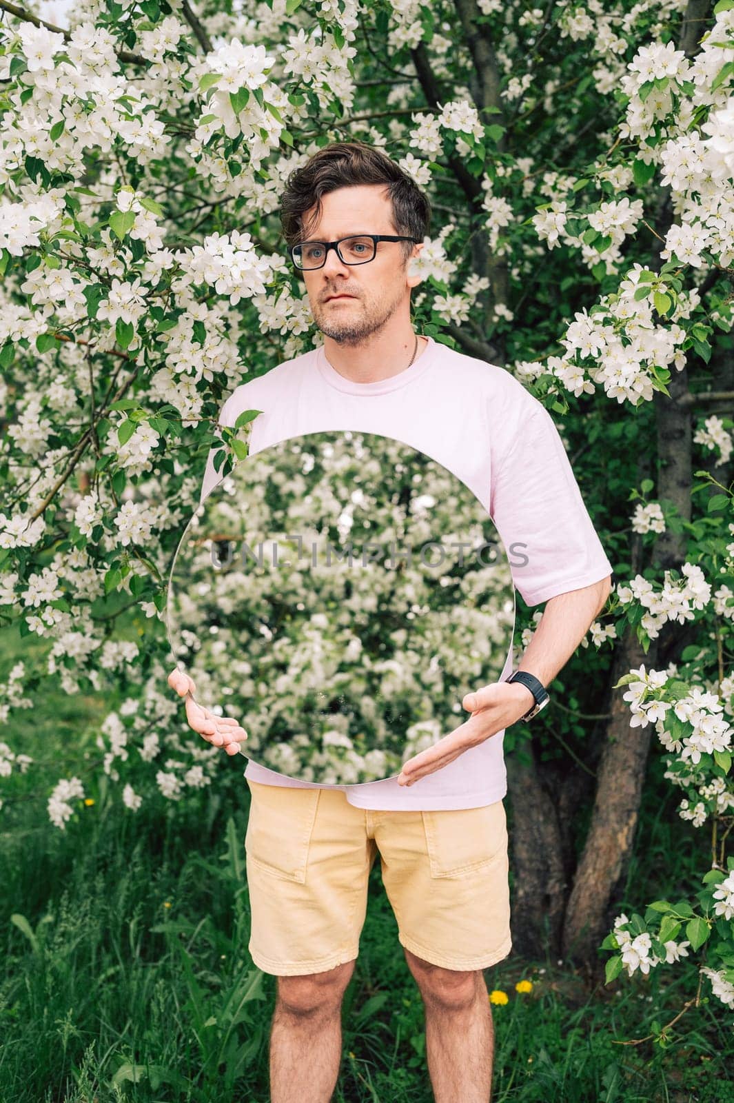 Creative male portrait with mirror in a blooming apples spring garden