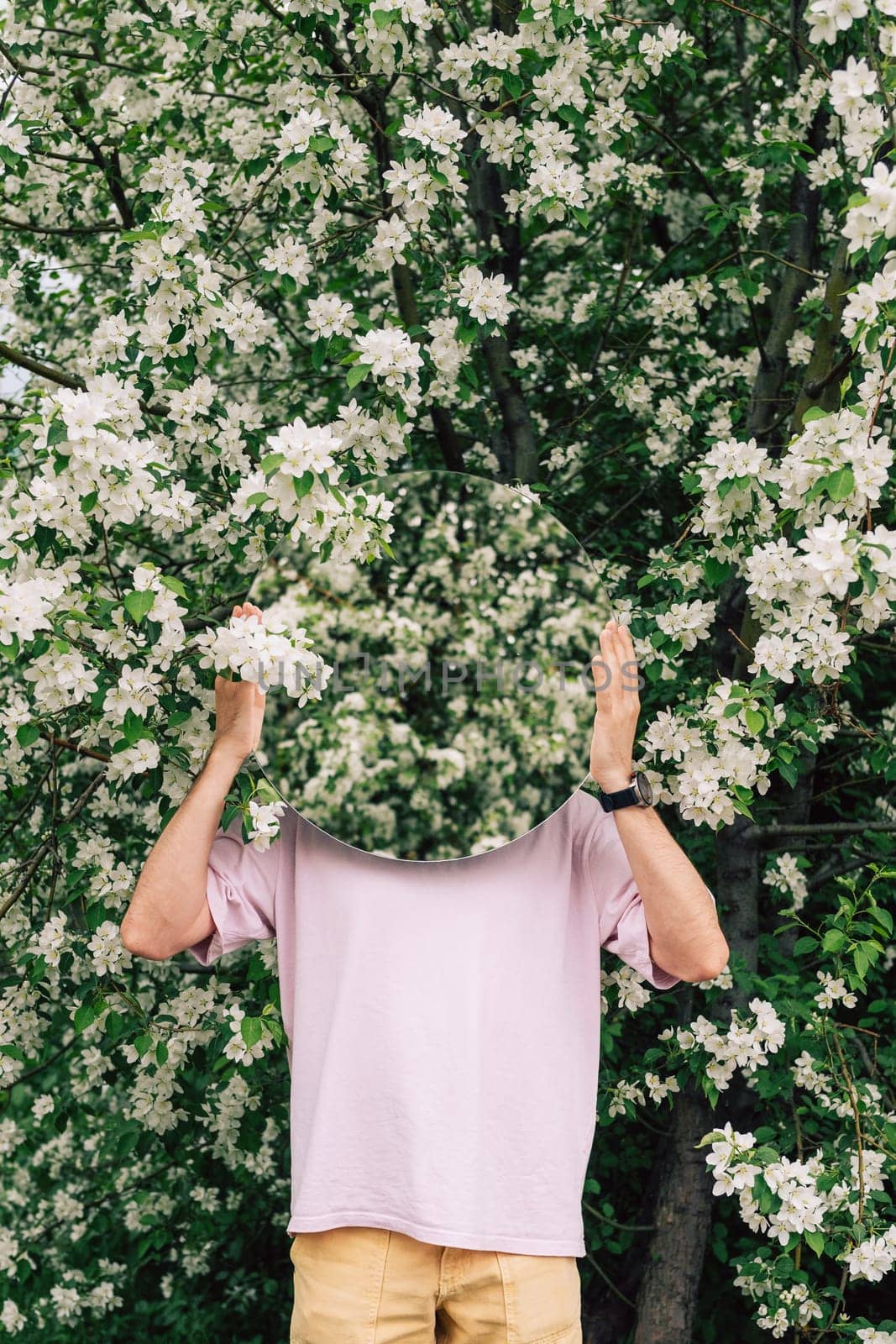 Creative male portrait with mirror in a blooming apples spring garden