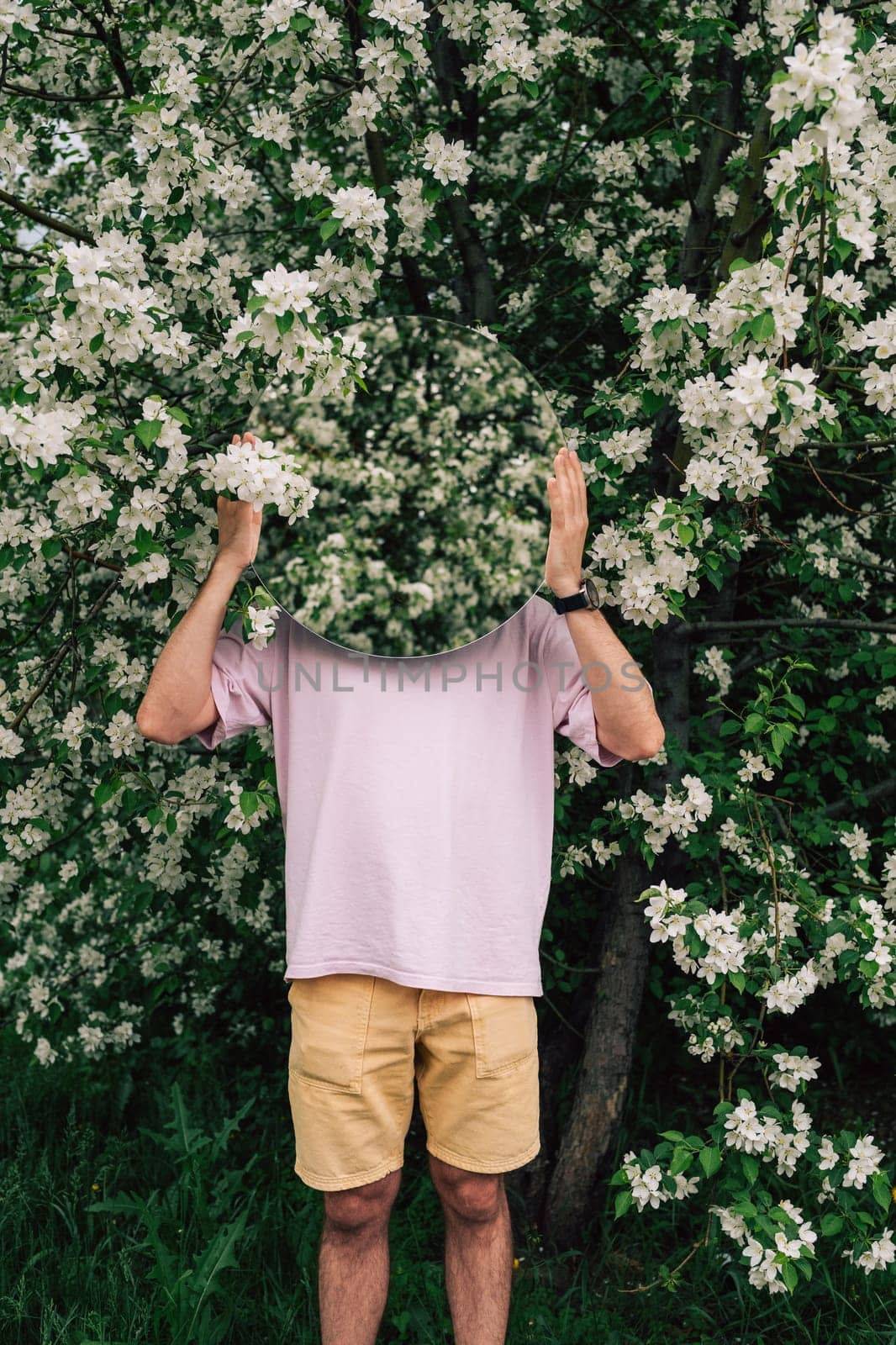 Creative male portrait with mirror in a blooming apples spring garden