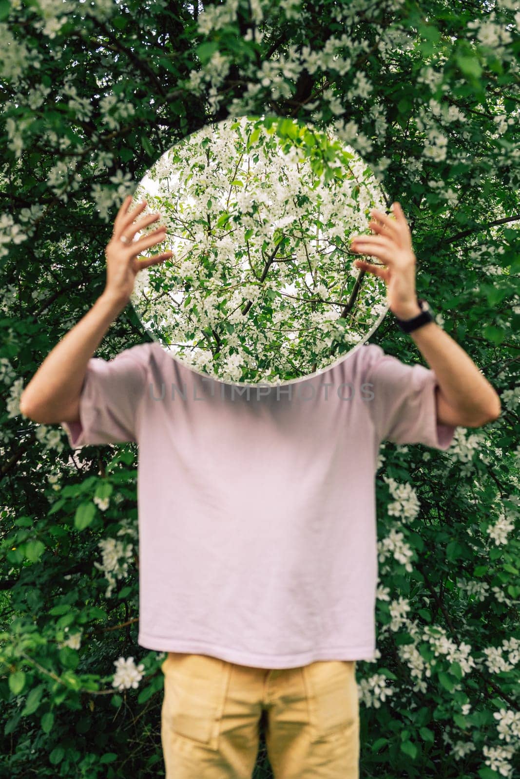 Creative male portrait with mirror in a blooming apples spring garden